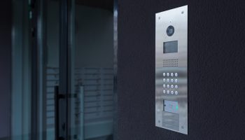 Entrance doorbell in a multi-apartment building, with a video surveillance camera, on a dark wall